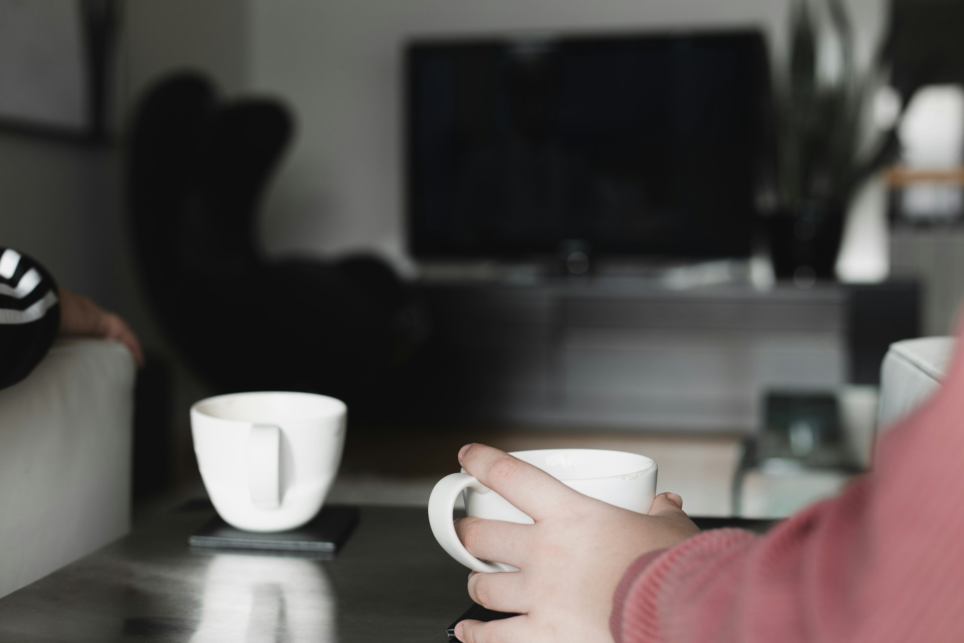 Vardagsrum med ett soffbord där det står två kaffekoppar som en person räcker sig efter.